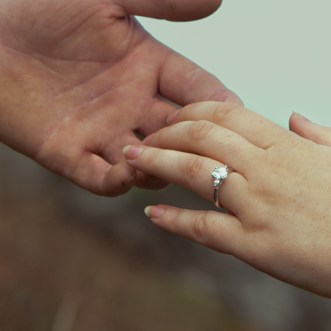 Close-up of a hand with a diamond ring being held by another hand against a blurred background