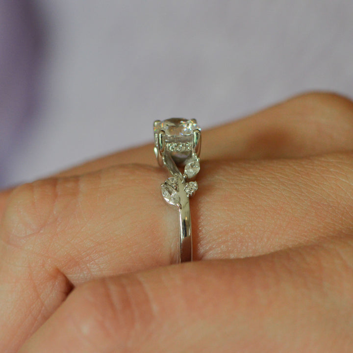 Side view of a hidden halo accented platinum ring set with diamonds, worn on the hand with a blurred background