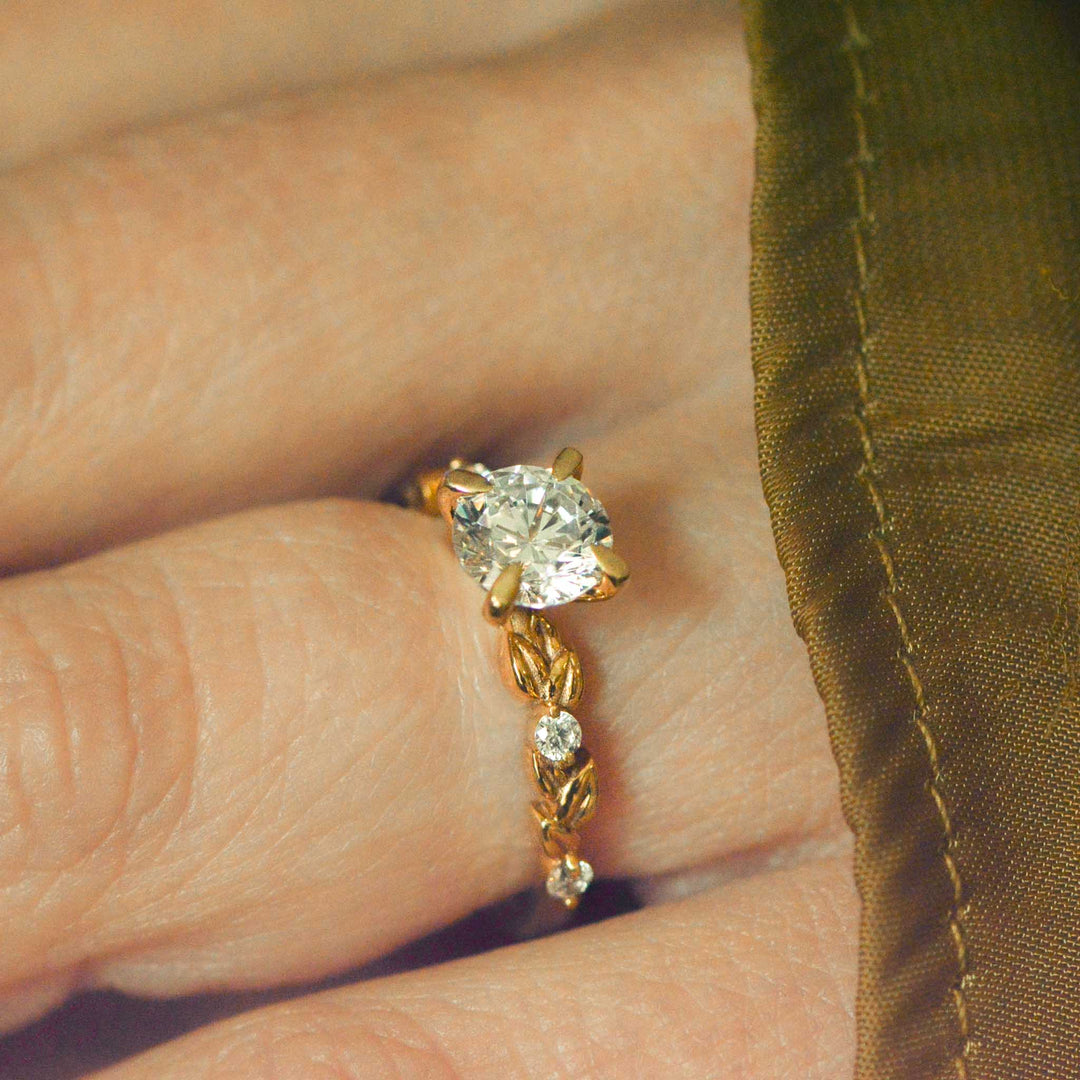 Gold nature inspired ring with a diamond on a hand against a green fabric background