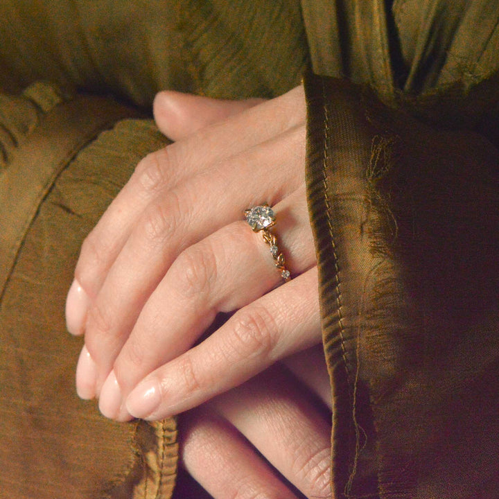 Close-up of a hand wearing a nature inspired round brilliant cut diamond ring with a textured brown background