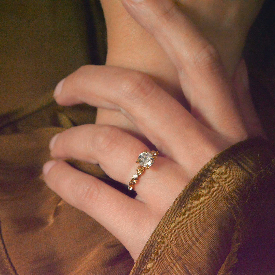 Close-up of a hand wearing a gold ring with a diamond on a brown background