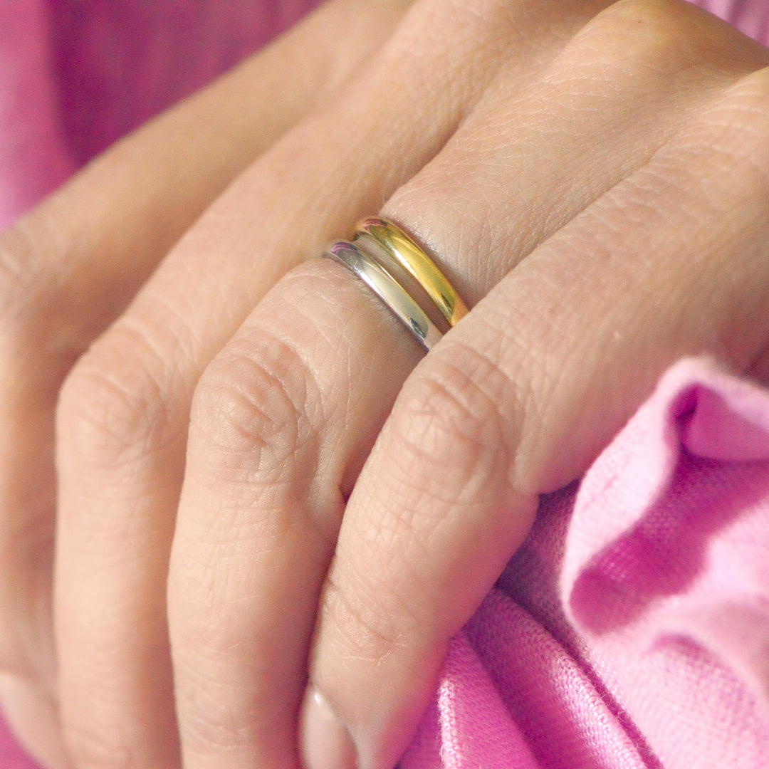 Close-up of a hand wearing two wedding bands with a pink background