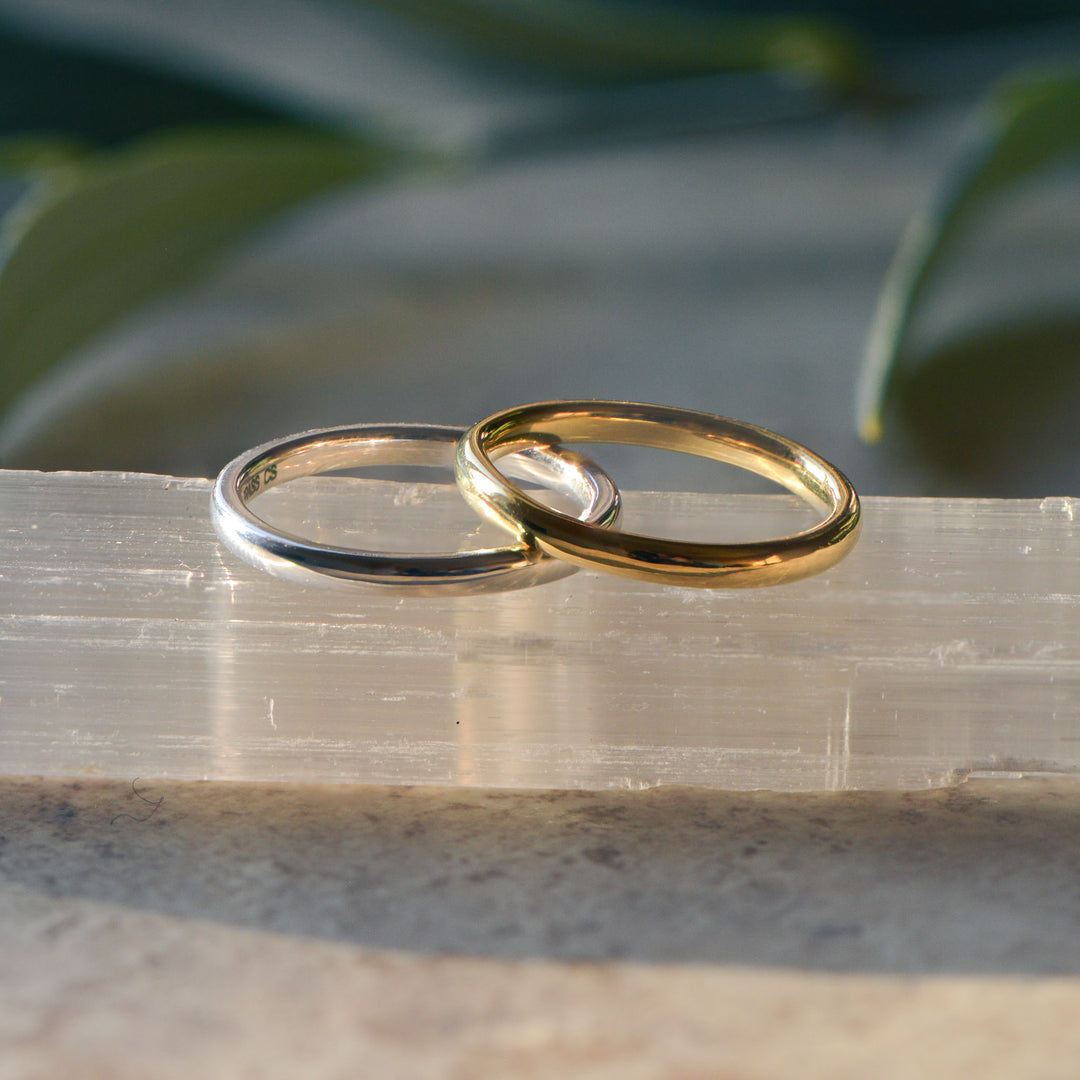 Two gold and platinum wedding bands on a clear crystal with green leaves in the background
