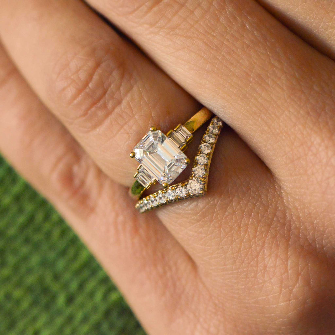 Gold Art Deco inspired ring with a large emerald cut diamond on a finger against a blurred green background