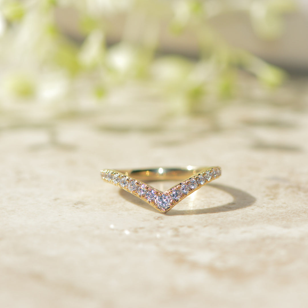 Gold chevron wedding band with pavé set diamonds on a marble surface