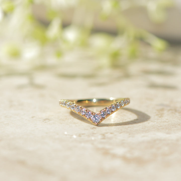 Gold chevron wedding band with pavé set diamonds on a marble surface