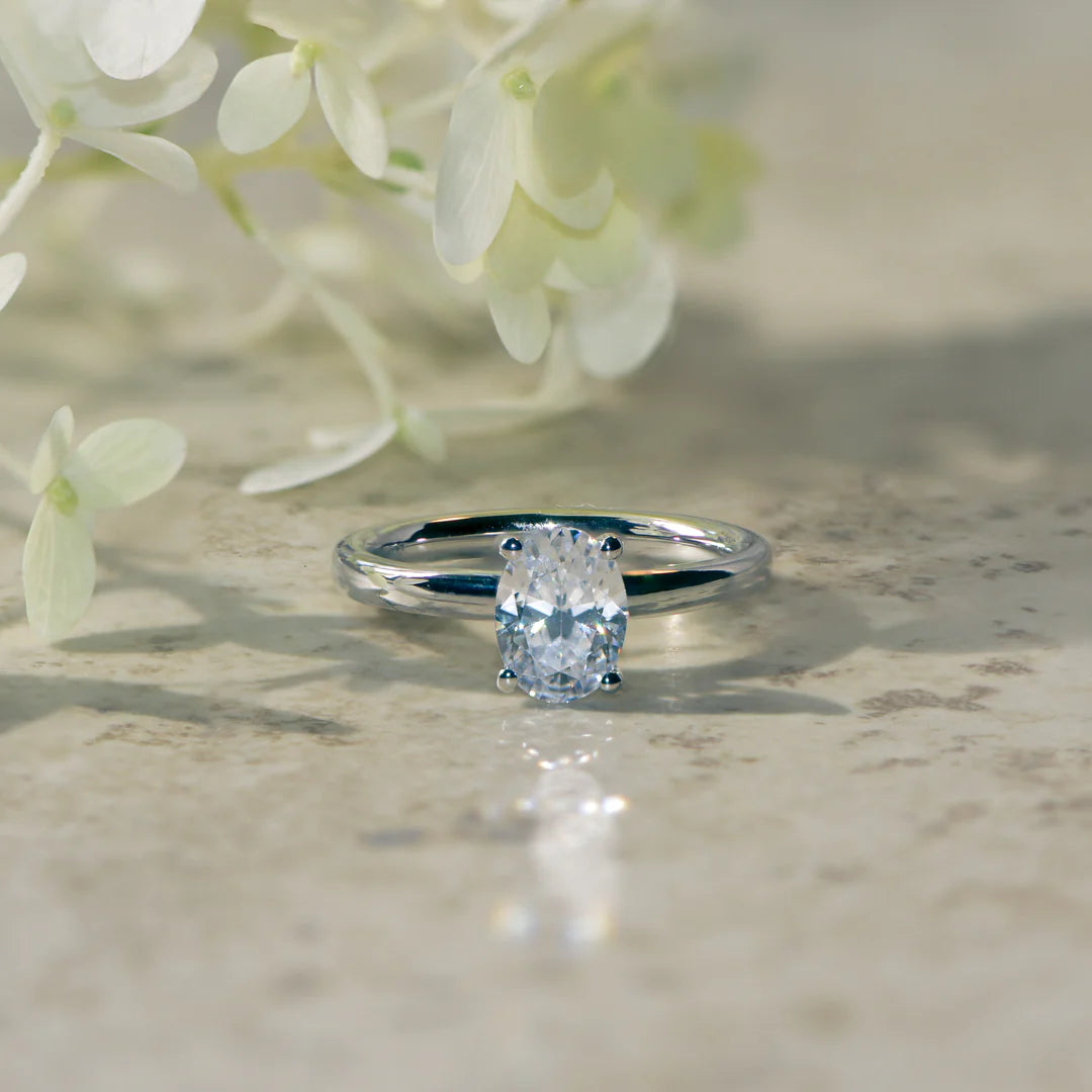 oval engagement ring set in platinum with a lab created diamond on a natural marble background. 