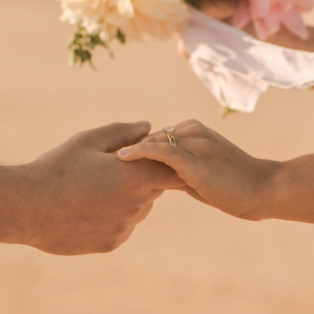 Close up of two hands on the beach with a diamond ring and gold wedding band 