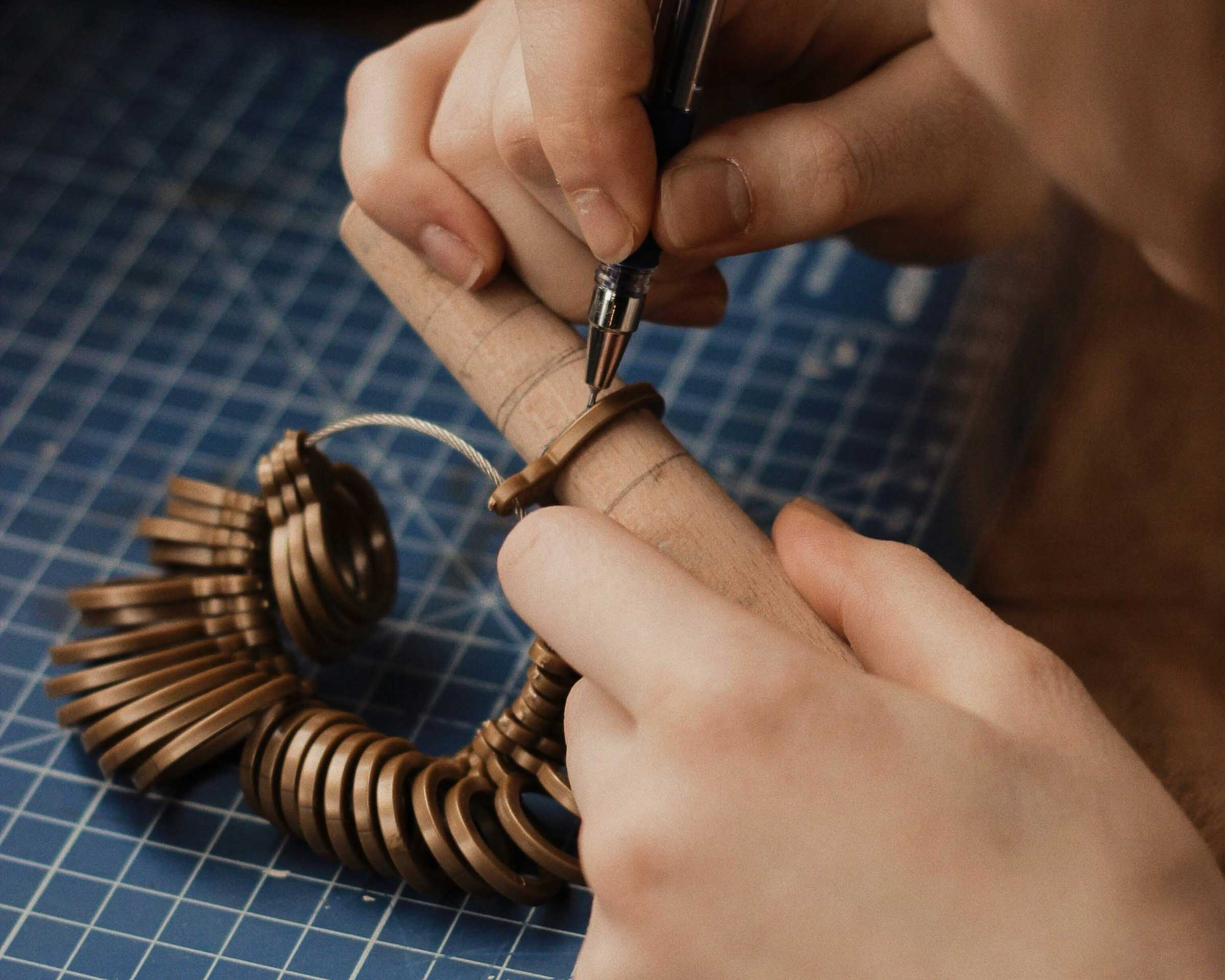 Person working on a ring resizing with a ring sizer on a blue grid surface