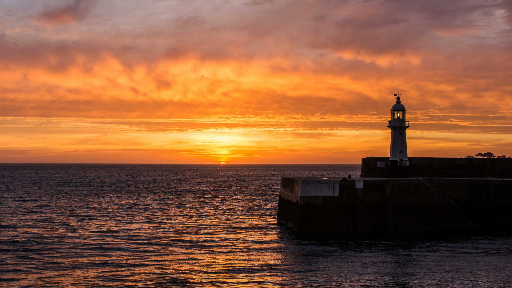 Lighthouse on a pier during a sunset with orange and purple hues in the sky.