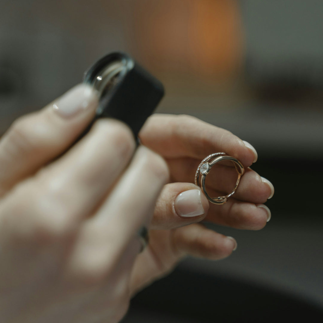 Hand holding a gold ring with a diamond and a jewellers loupe  against a blurred background