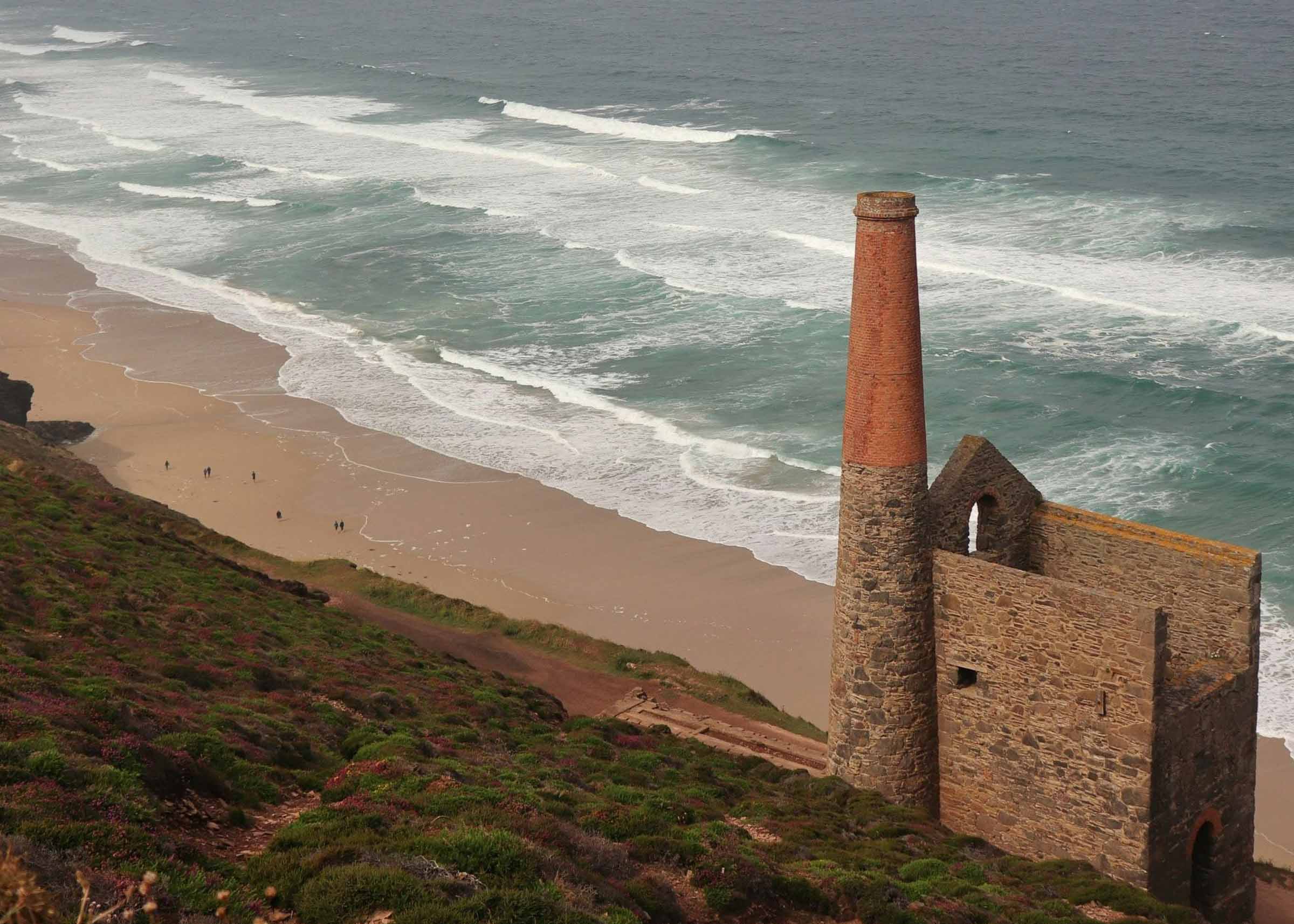 Ruin of Cornish tin mine on a beach with ocean waves crashing against it
