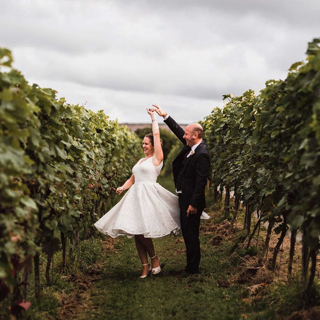 Couple dancing on their wedding day at Trevibban Mill Vineyard among rows of grapevines on a cloudy day.